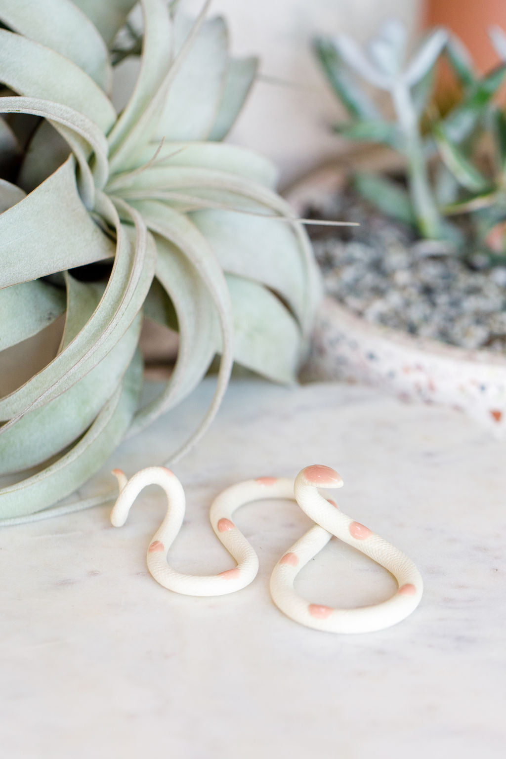 Small organic s-shaped pottery snake sculpture in the colorway Sofie, ivory white clay body with a light pink glazed head and evenly spaced glazed dots along its body.