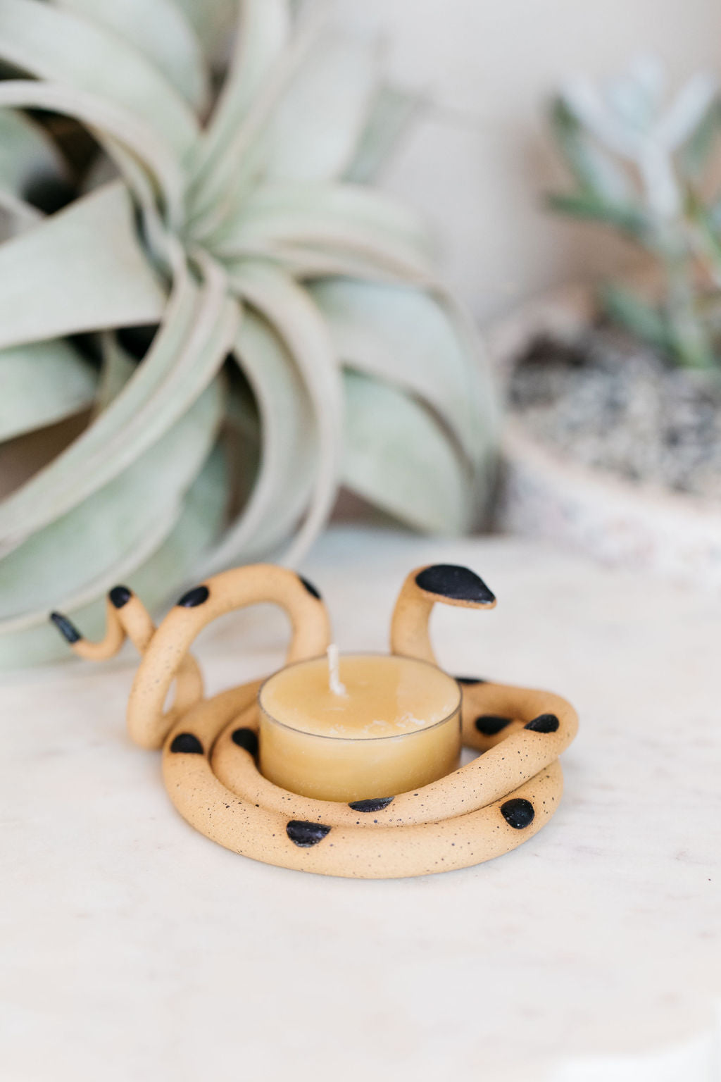 Organically coiled black clay snake with black head and dots. This colorway is Saul. Styled with a beeswax tea light that sits in the center of the coil.