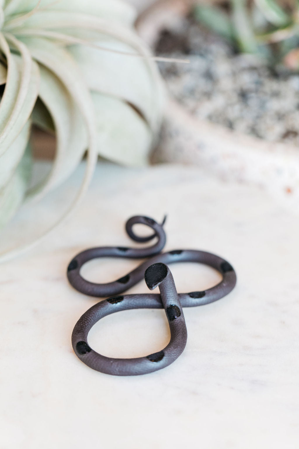 Small organic s-shaped pottery snake sculpture in the colorway Saul, matte black clay body with a black glazed head and evenly spaced glazed dots along its body.