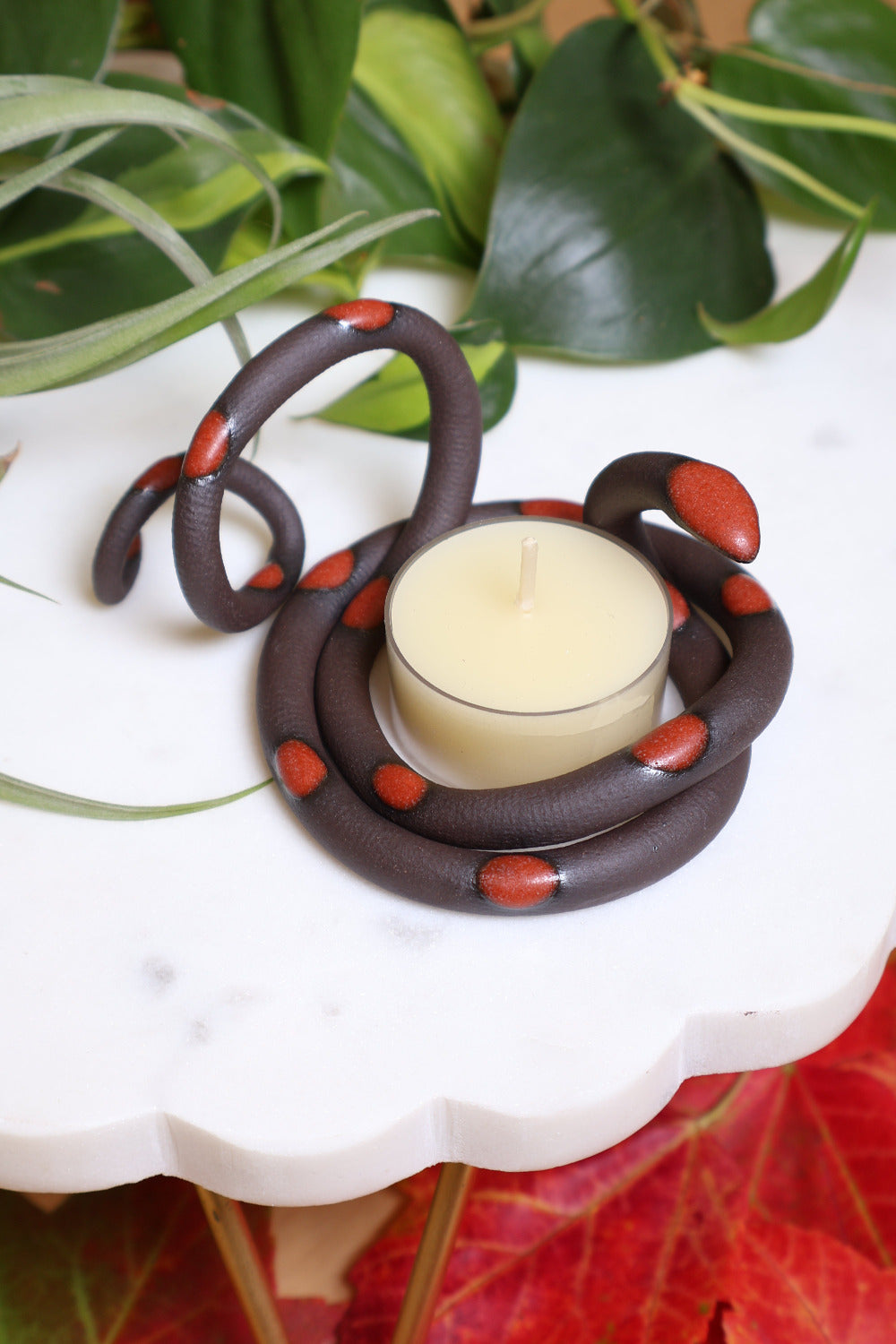 Organically coiled black clay snake with red-orange glazed head and dots. This colorway is Squash. Styled with a beeswax tea light that sits in the center of the coil. 