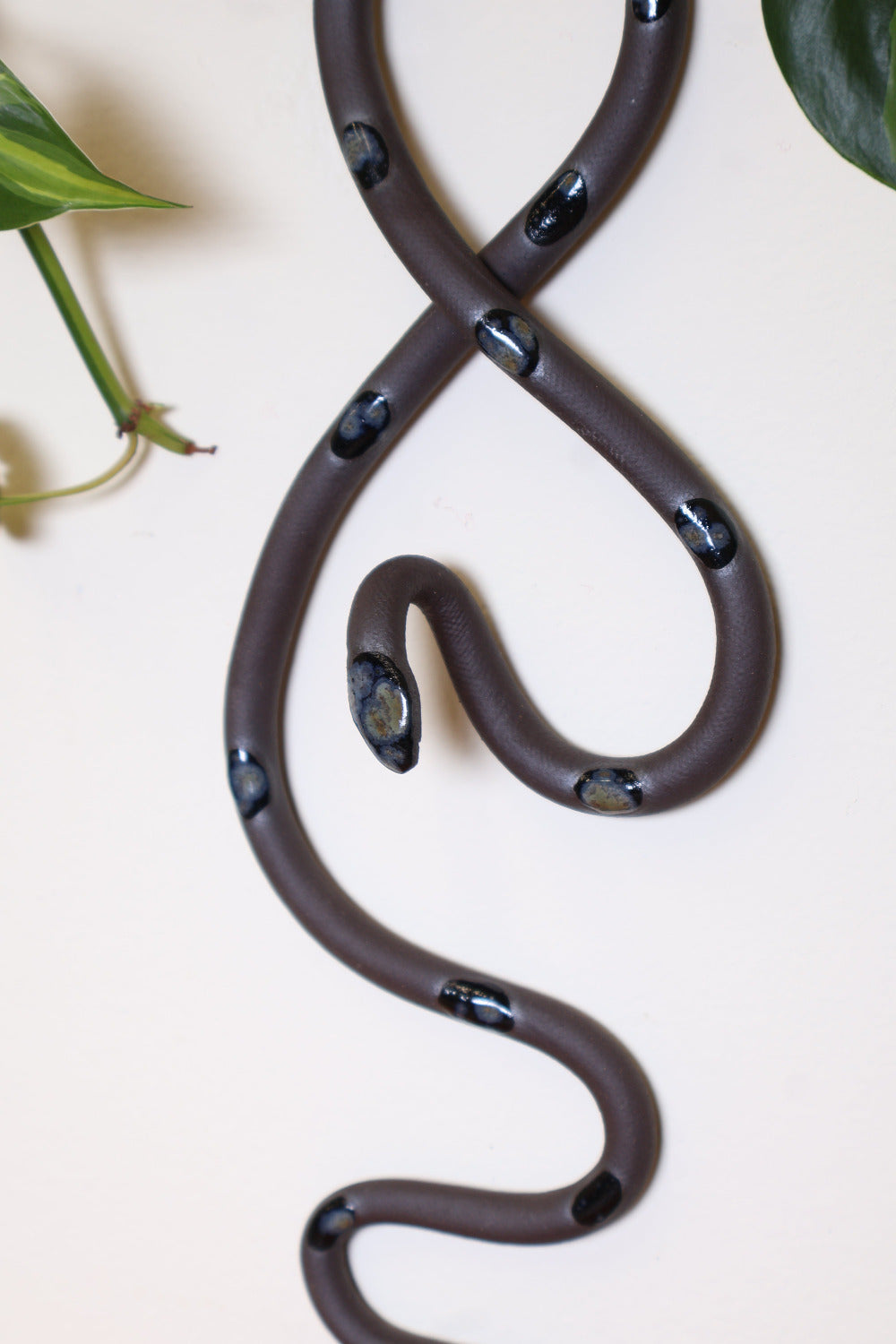 Close up of the black crystalline burst glaze dots on the Shadow wall snake. The dots are on dark chocolate colored clay and are glossy with some dark umber, gray and navy splashes of color. 