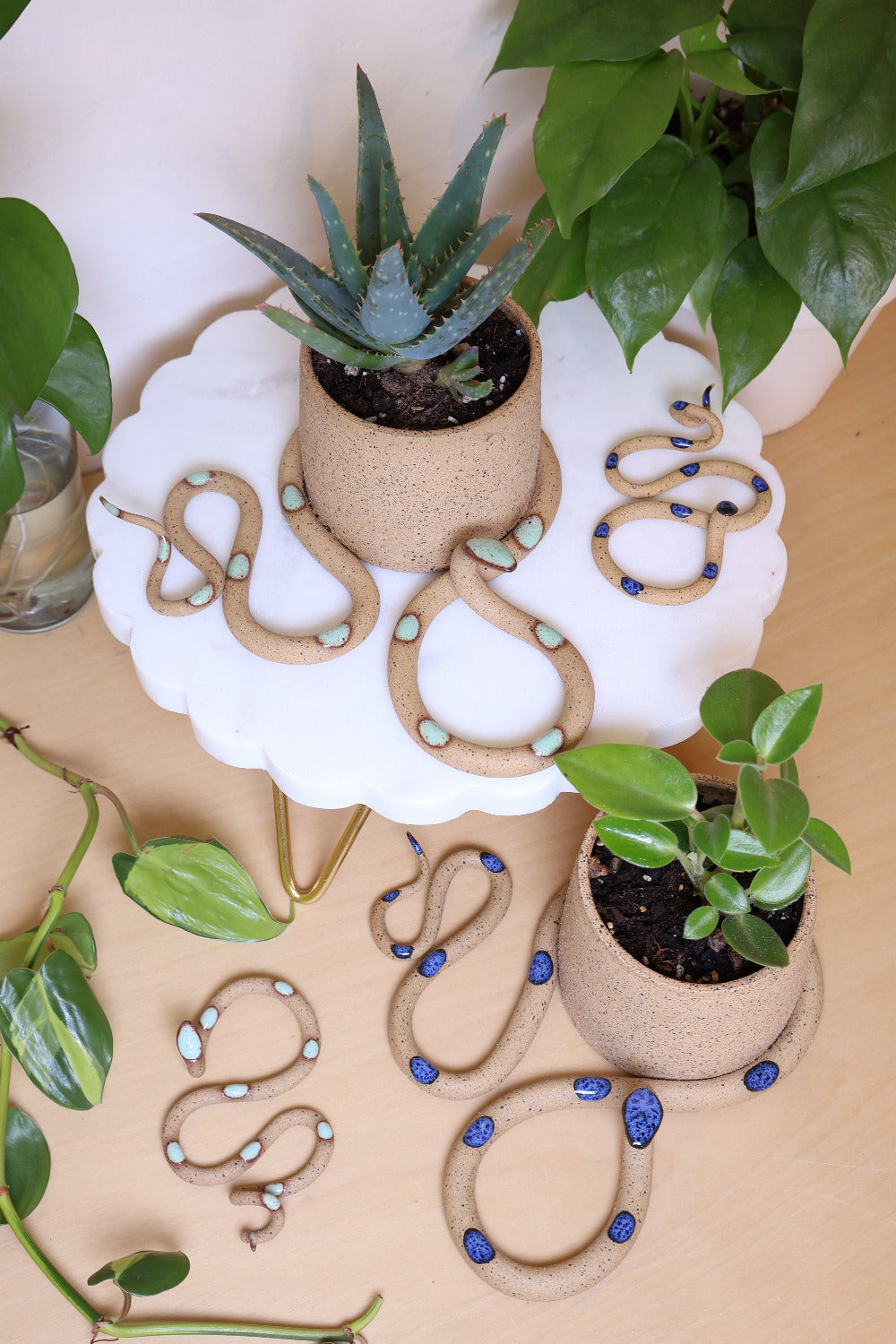 Styled snake pots with potted plants, surrounded by small ceramic snakes and house plants. 