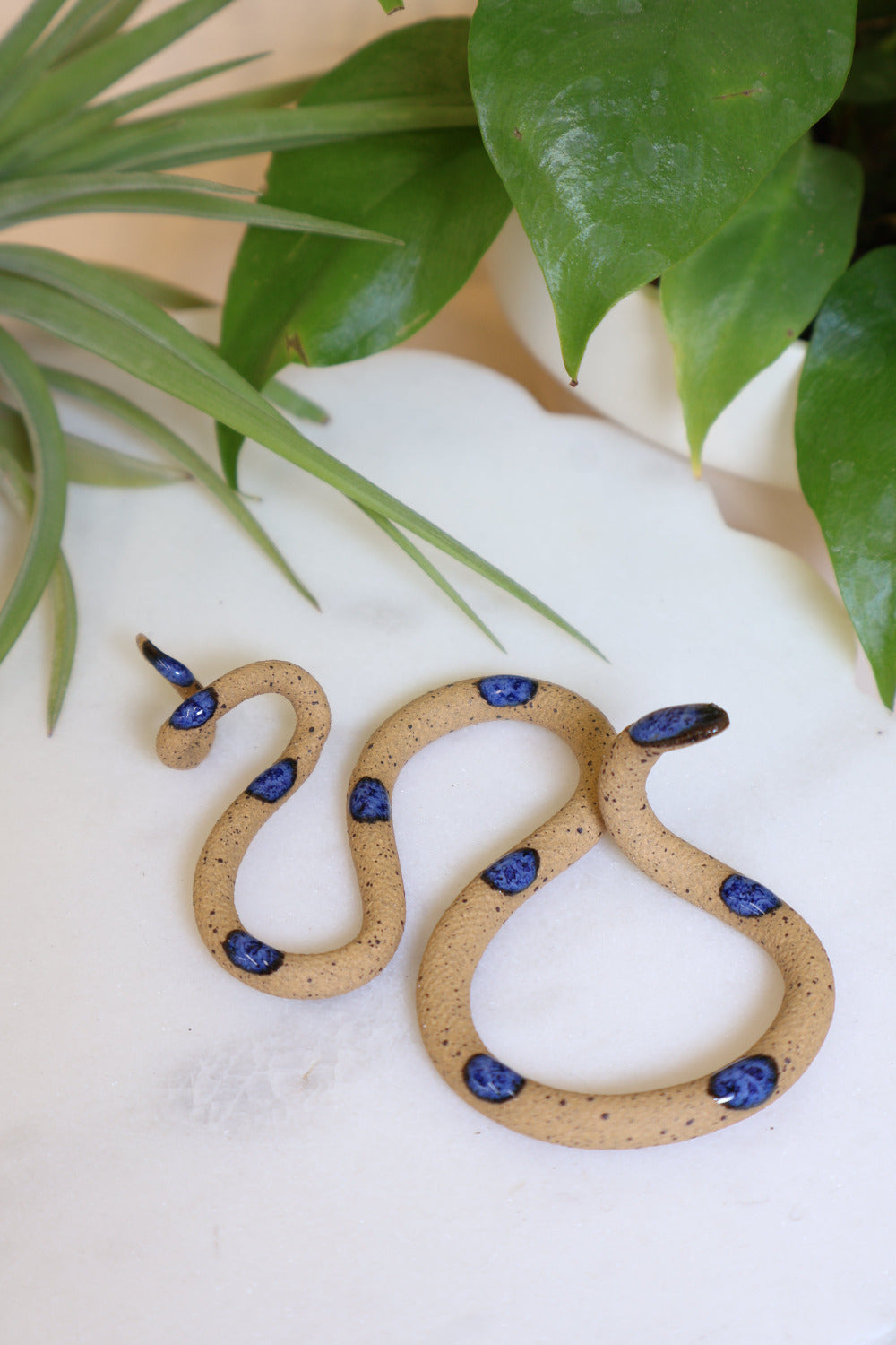Small organic s-shaped pottery snake sculpture in the colorway Selena, a speckled tan clay body with a deep blue glazed head and evenly spaced glazed dots.