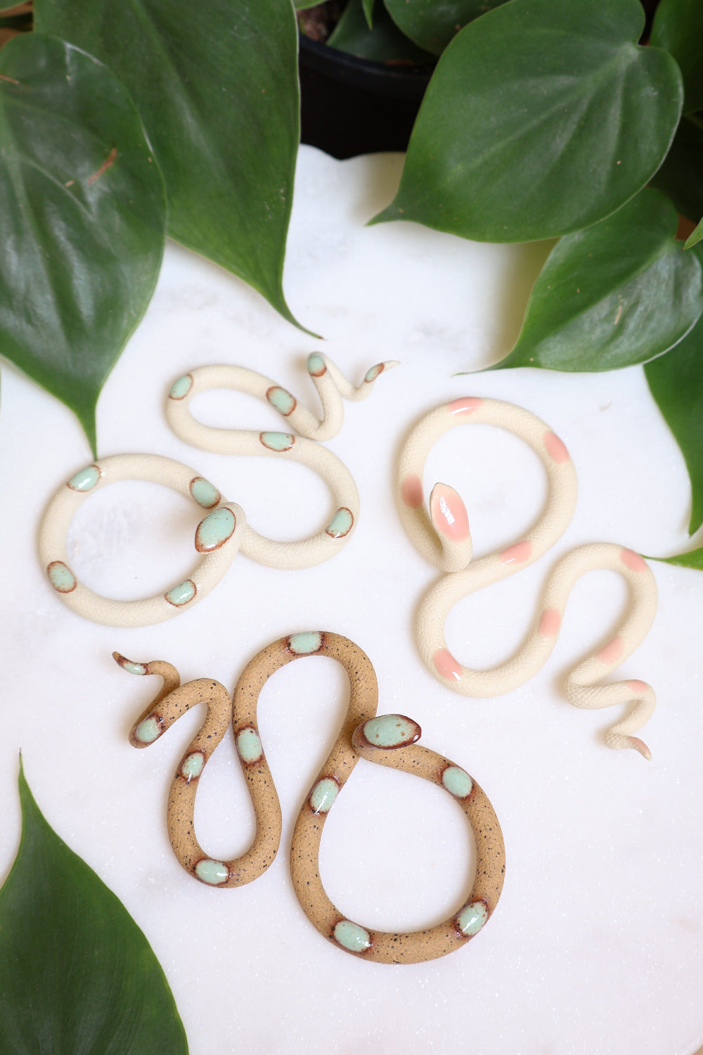 Garden curated set of three small ceramic snakes in the following colorways, Sylvia (ivory clay with light turquoise glaze dots), Sofie (ivory clay with light pink glaze dots), and Selma (speckled clay with turquoise glaze dots).