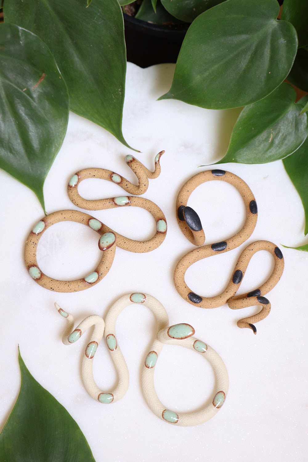 Desert curated set of three small ceramic snakes in the following colorways, Selma (speckled tan clay with light turquoise glaze dots), Sammy (speckled tan with black glaze dots) and Sylvia (ivory clay with light turquoise glaze dots).