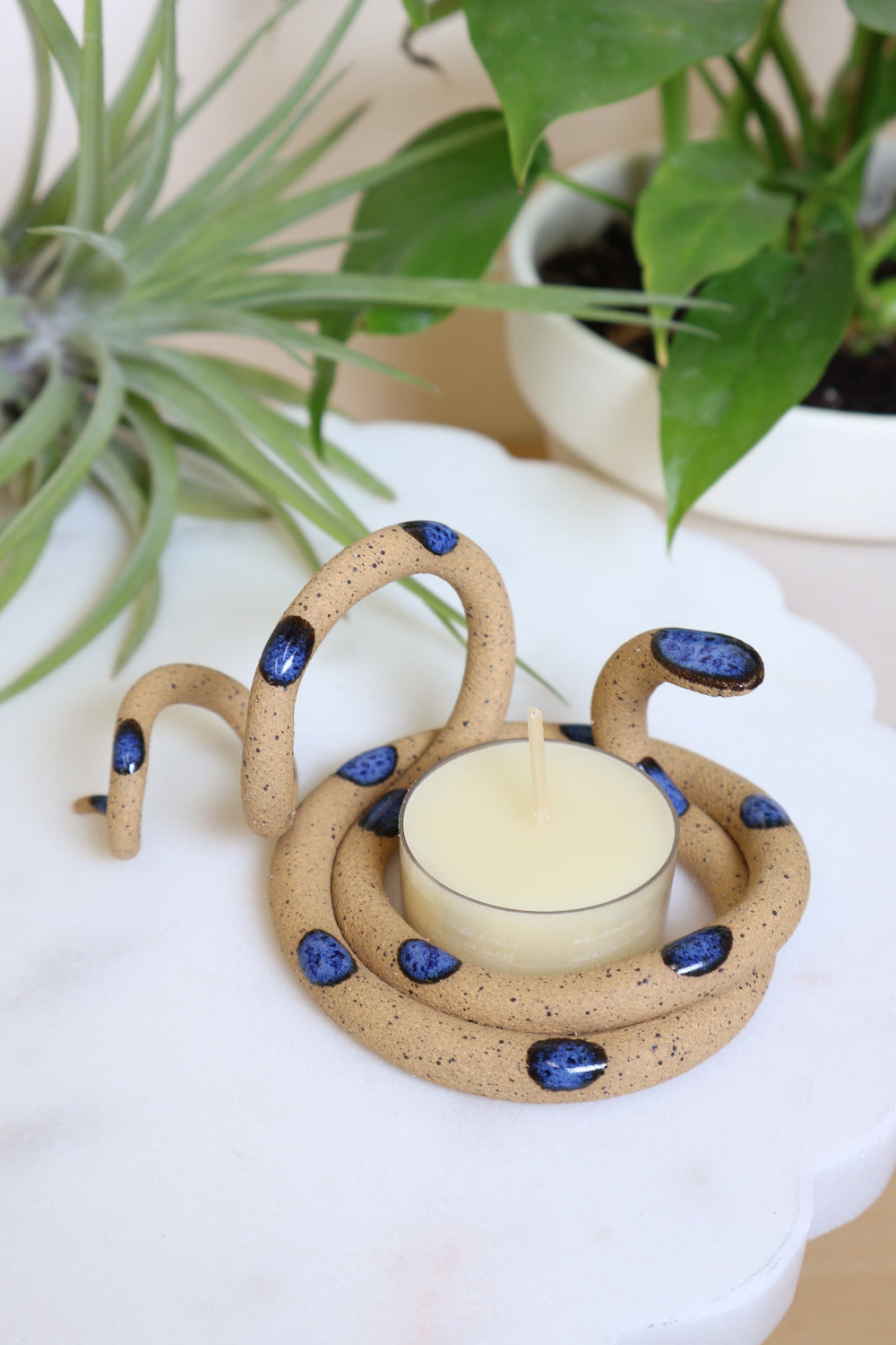 Organically coiled speckled tan clay snake with blue head and dots. This colorway is Selena. Styled with a beeswax tea light that sits in the center of the coil.