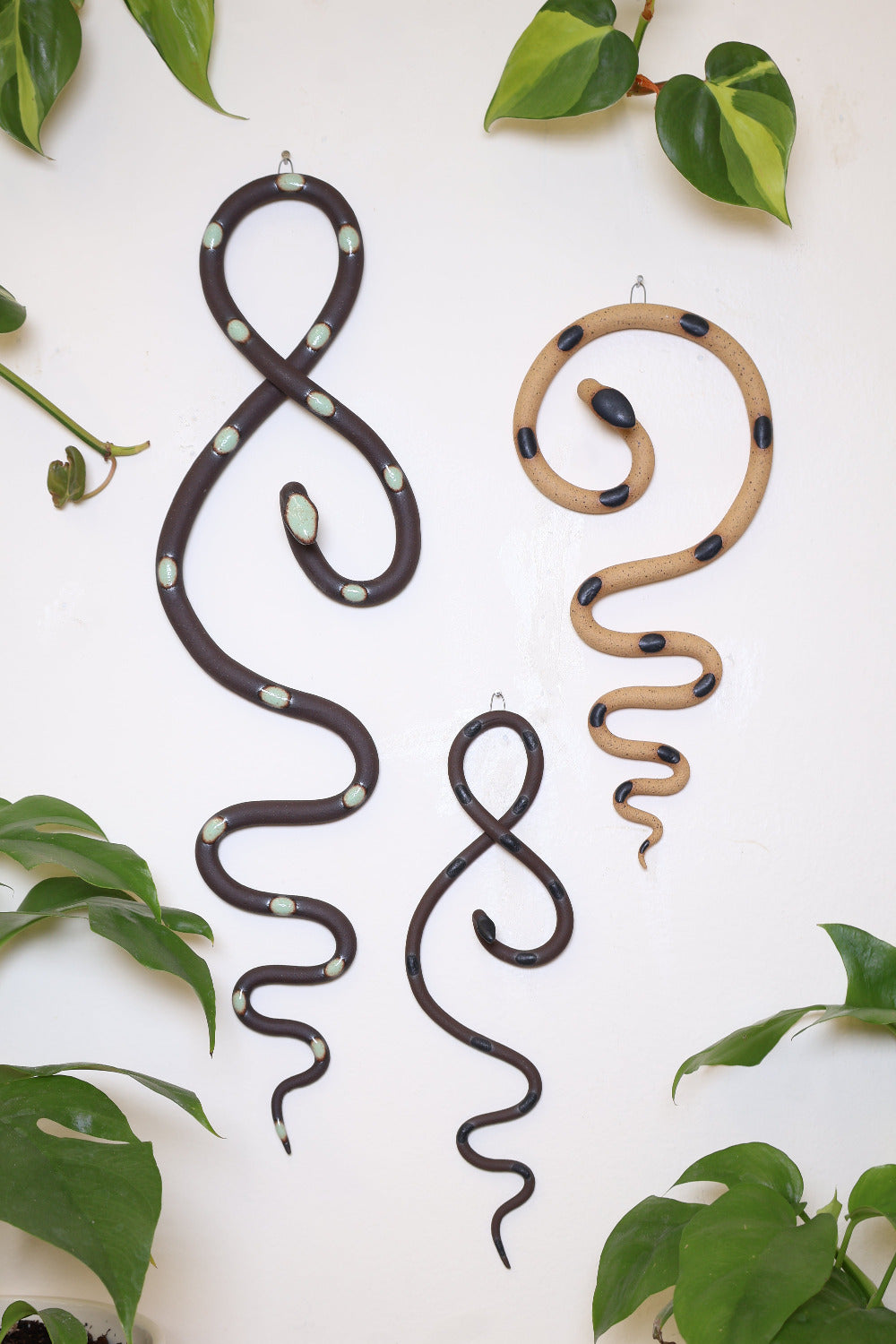 Desert curated set of three wall ceramic snakes. From left to right hanging on a wall is a Selma wall snake (tan clay, turquoise dots), Sammy mini wall snake (tan clay, black dots), and a medium Sylvia wall snake (white clay, turquoise dots).