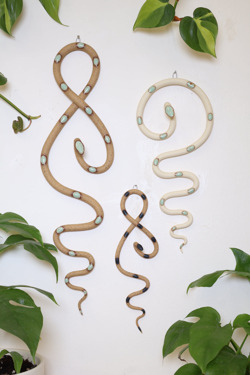 Desert curated set of three wall ceramic snakes. From left to right hanging on a wall is a Selma wall snake (tan clay, turquoise dots), Sammy mini wall snake (tan clay, black dots), and a medium Sylvia wall snake (white clay, turquoise dots).