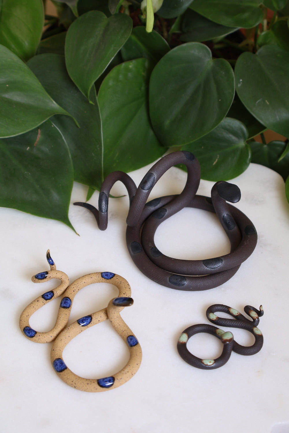 Set of three ceramic snake sculptures featuring a medium Saul (dark chocolate clay with black dots), a small Selena (speckled clay with blue dots) and a baby Stevie (dark chocolate clay with turquoise dots). This is the Marsh set. 