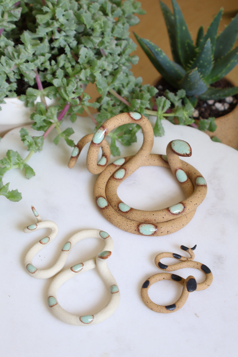 Set of three ceramic snake sculptures featuring a medium Selma (speckled clay with turquoise dots), a small Sylvia (ivory clay with turquoise dots) and a baby Sammy (speckled clay with black dots). This is the Desert set.
