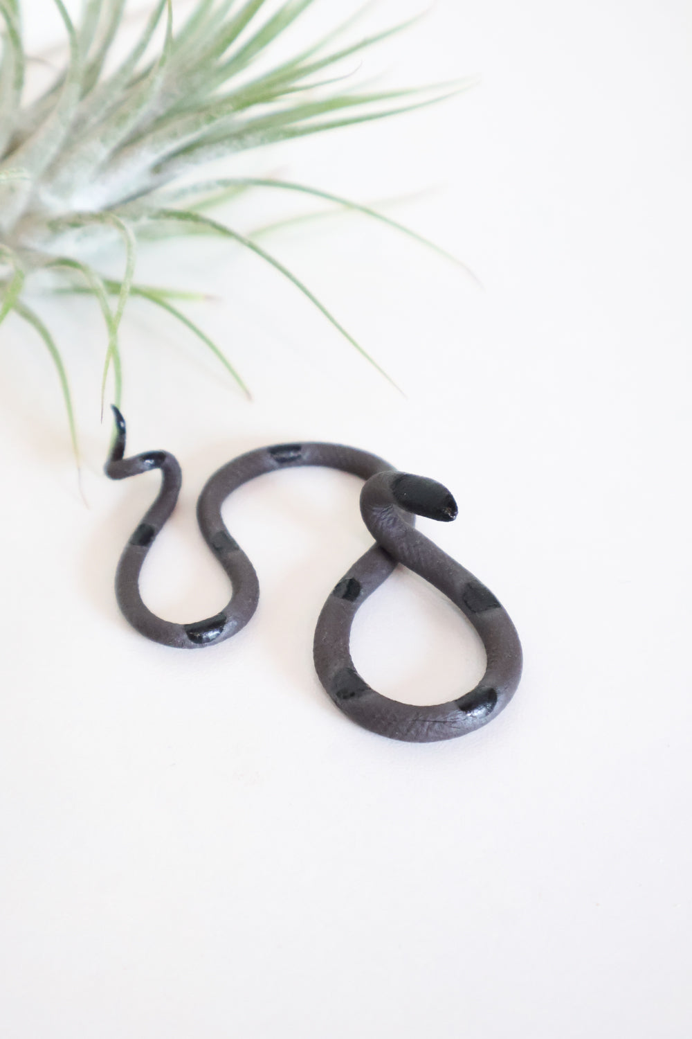 Itty bitty organic s-shaped pottery snake sculpture in the colorway Saul, matte black clay body with a black glazed head and evenly spaced glazed dots along its body.