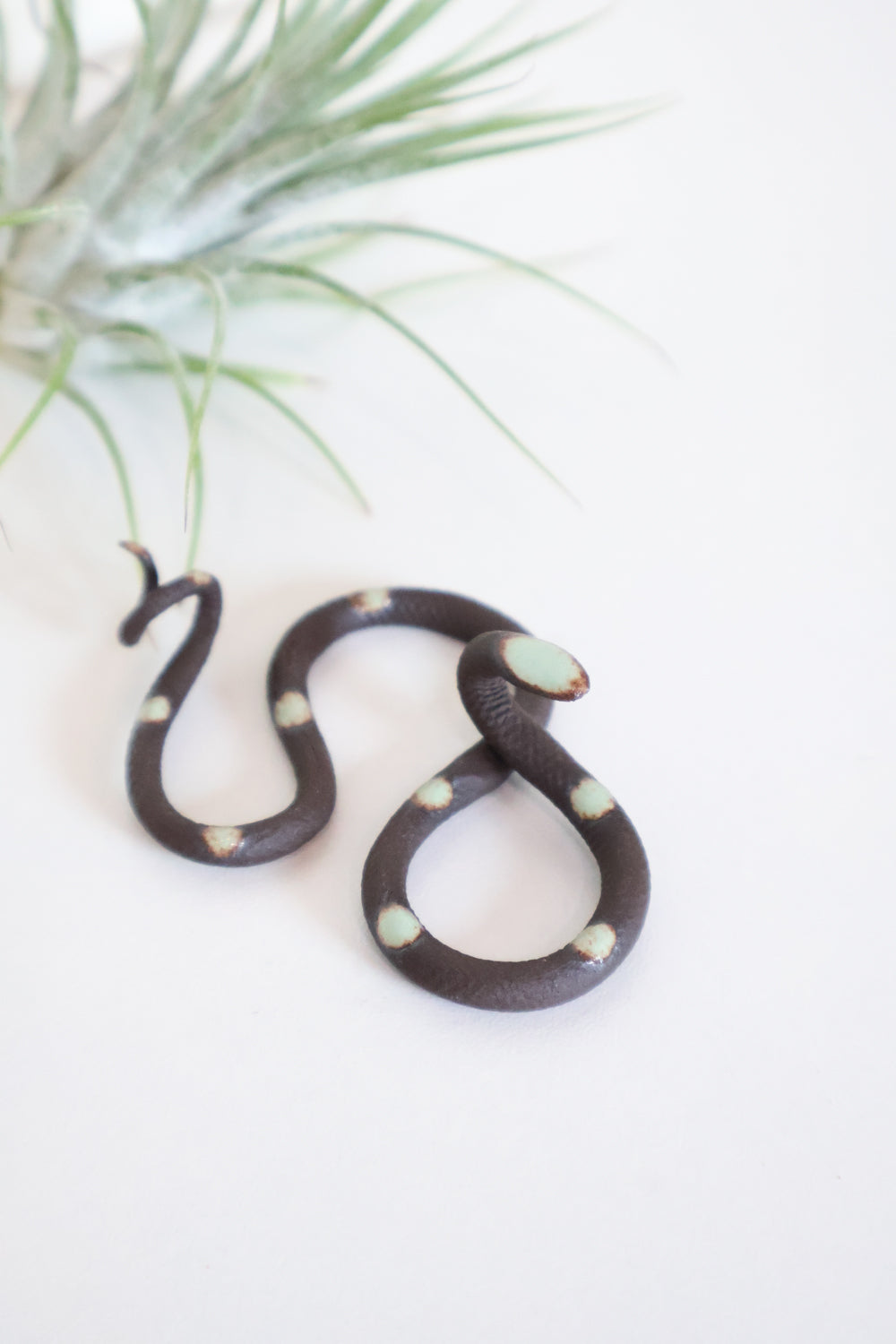 Itty bitty organic s-shaped pottery snake sculpture in the colorway Stevie, a matte black clay body with a light turquoise glazed head and evenly spaced glazed dots.