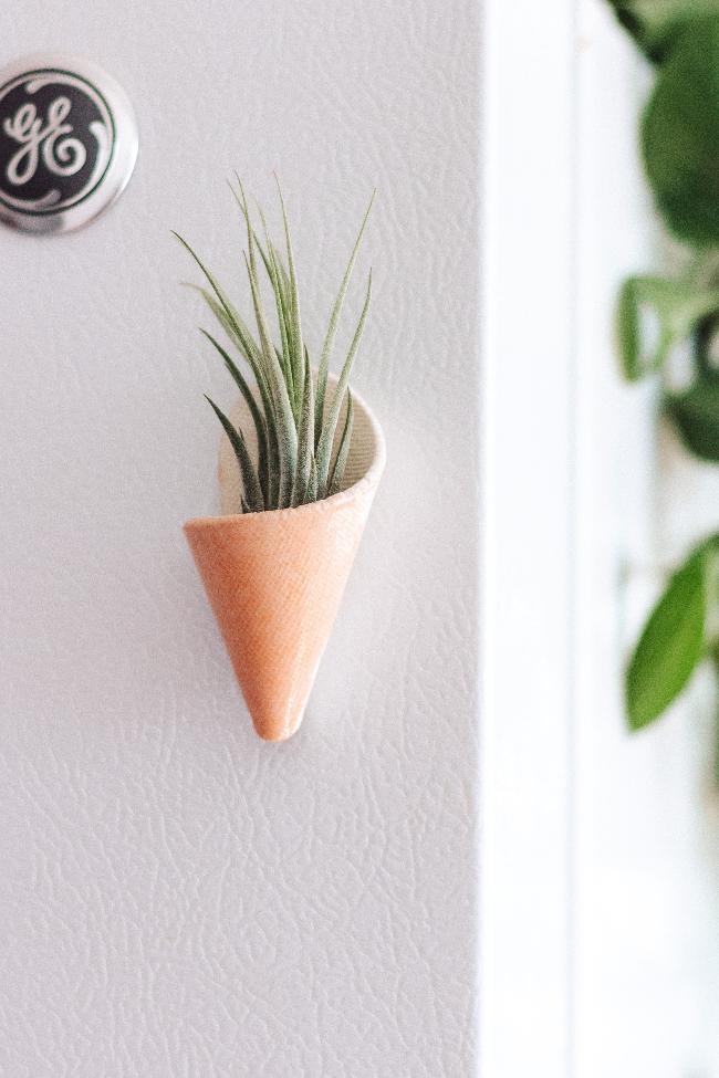 Small pastel pink ceramic magnetic cone. The cone is styled sticking to a fridge and is holding an air plant. 