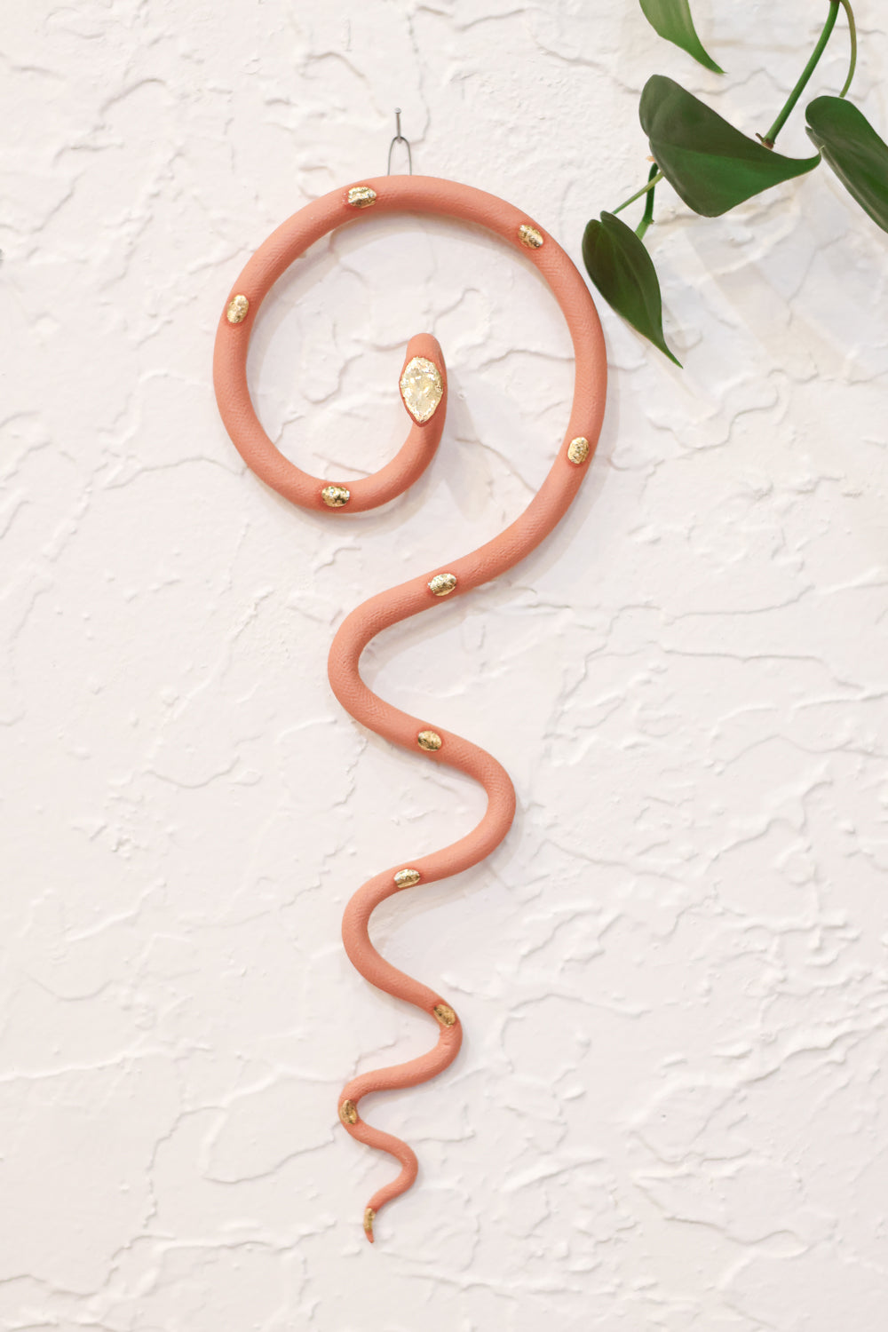 Light terracotta coiled pottery wall snake with gold glazed head and dots. The snake is shaped loosely like a question mark with the tail hanging down in an organic s curve. This colorway is desert sand.