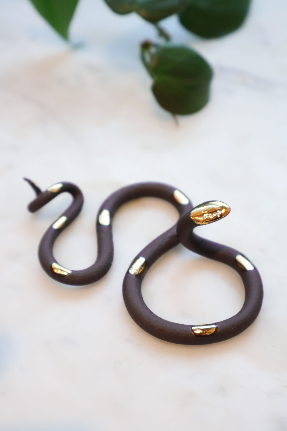 Black midnight small organic s-shaped clay snake sculpture with a black clay body and gold glazed head and spots. 