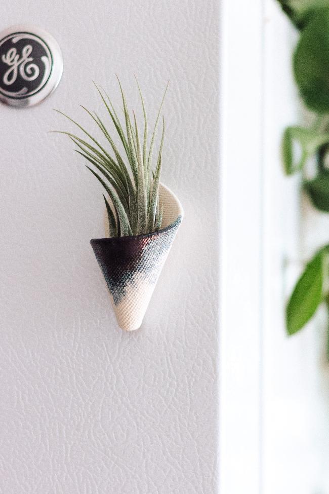 Small white magnetic ceramic cone with indigo glaze brushed in in a triangle at the top of the cone. The cone is styled sticking to a fridge and is holding an air plant. 