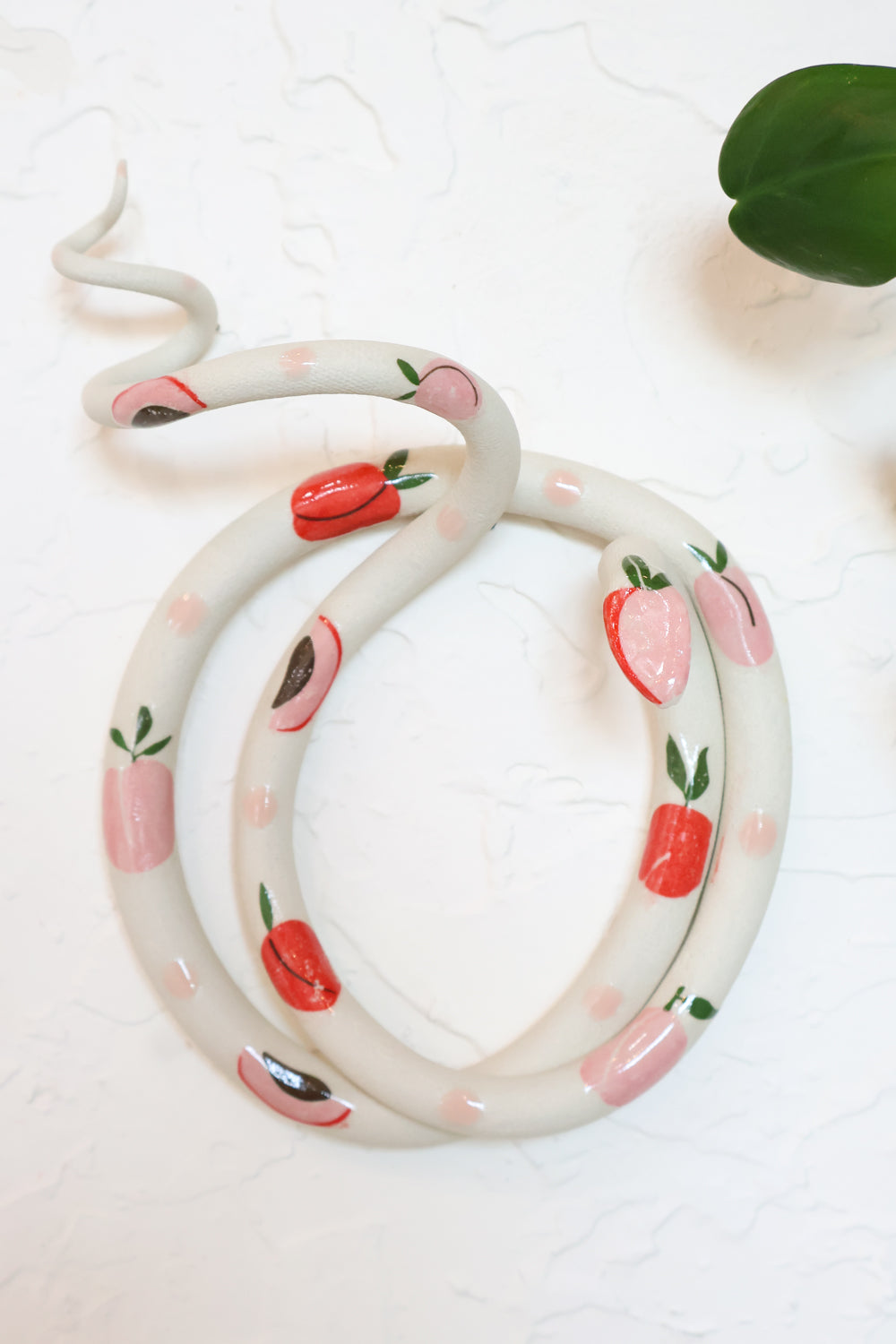 Ivory clay snake with black speckles and pink and red strawberries. The snake is coiled in a circle with it's head raised and tail in a spiral