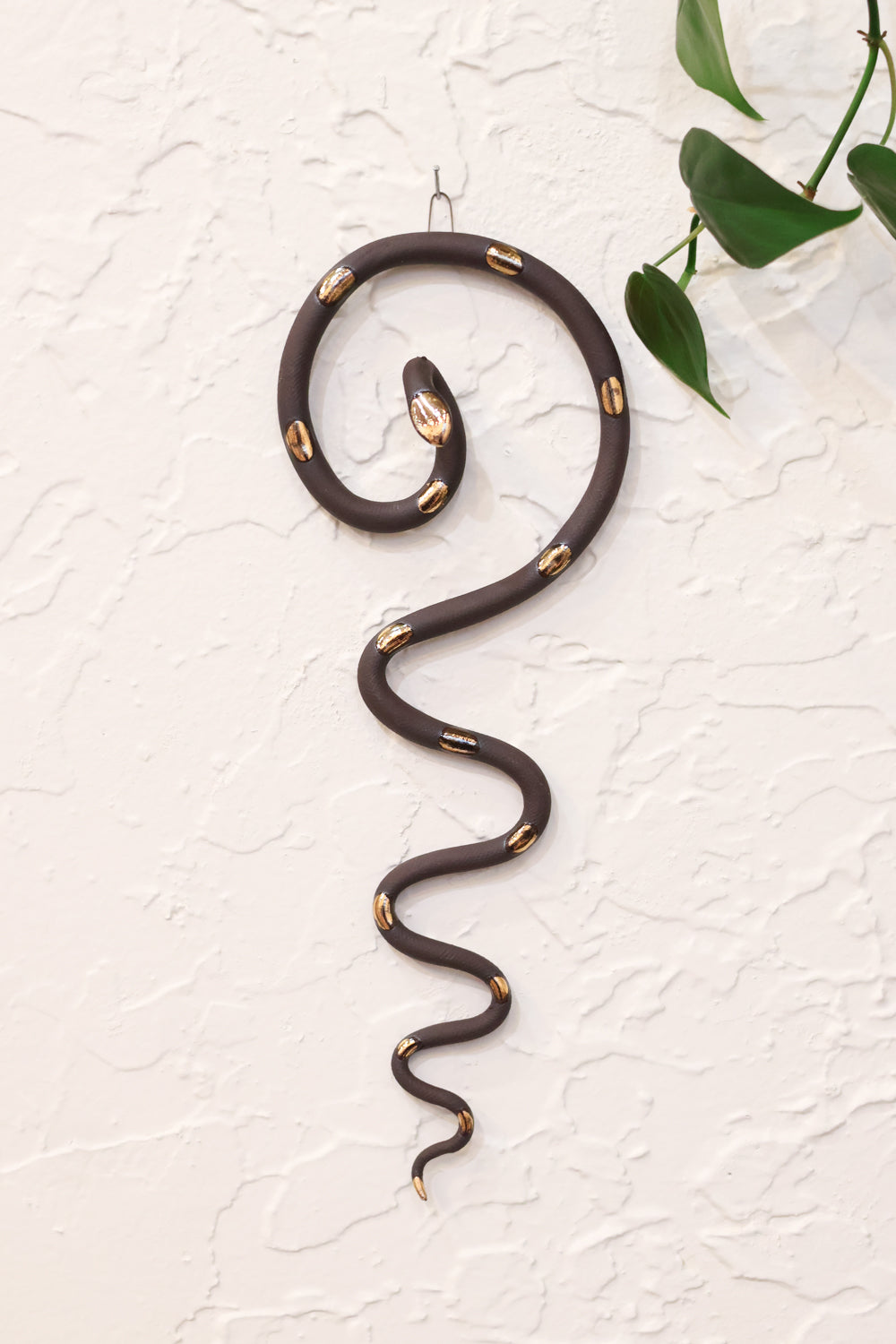 Black coiled pottery wall snake with gold glazed head and dots. The snake is shaped loosely like a question mark with the tail hanging down in an organic s curve. 