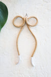 A minimalist ceramic shoelace style bow ornament made of speckled beige clay with curved, white-tipped ends. 