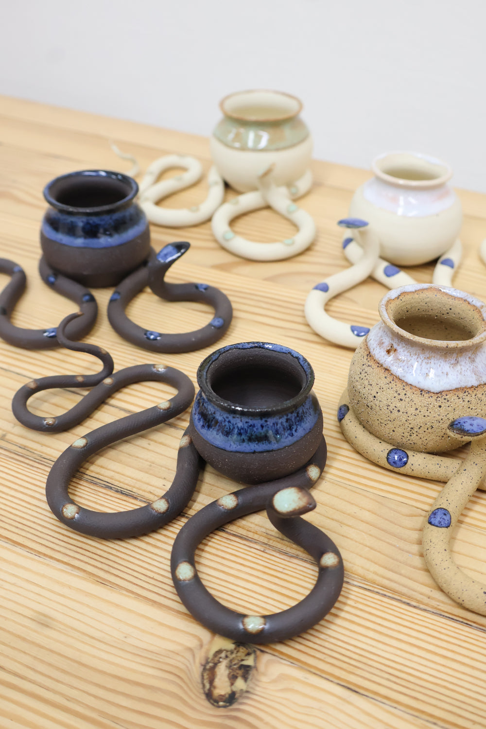 Four clay tabletop snake sculptures with tight s-curved body and raised head. There is a small round vase nestled in the second curve that can be used for an air plant, or dried flowers. 