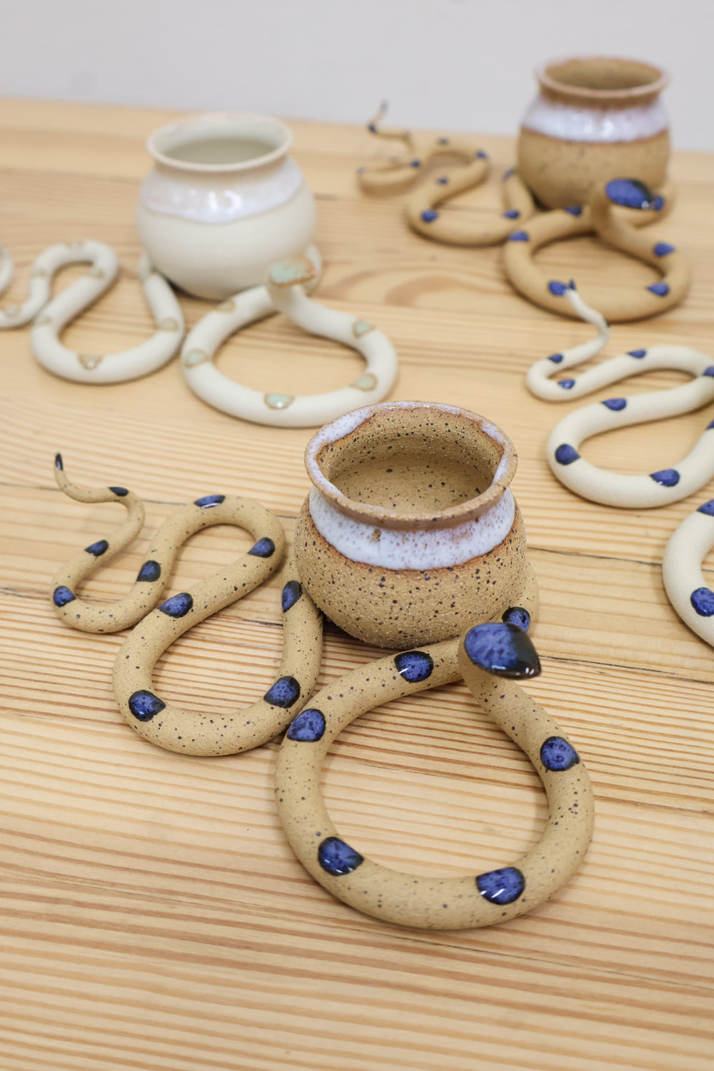 Four clay tabletop snake sculptures with tight s-curved body and raised head. There is a small round vase nestled in the second curve that can be used for an air plant, or dried flowers. 