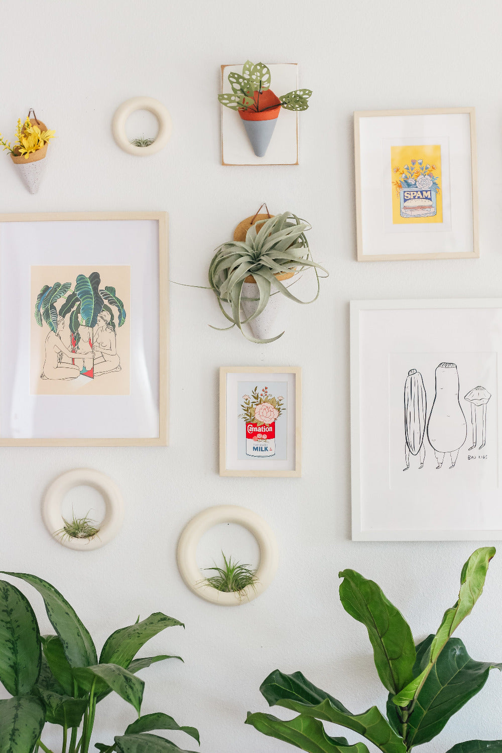 A speckled white jumbo cone centered on a gallery wall of various framed art and ceramics. The cone is styled with a large xerographica air plant.
